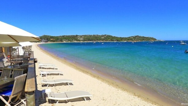 A beach with clear blue water, a sandy shore, and lounge chairs. - GARDEN VILLA 3 MINUTES WALK FROM CALA ROSSA BEACH - RESIDENCE MARINA ROSSA (Lecci)