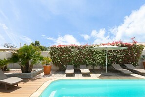 A poolside area with lounge chairs, a small pool, and a wall covered with flowering plants.