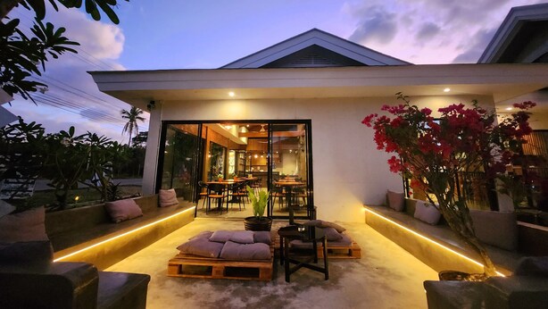 An outdoor seating area with a dining space visible through glass doors, surrounded by plants and a modern architectural design. - Only Seed Resort (Panglao)