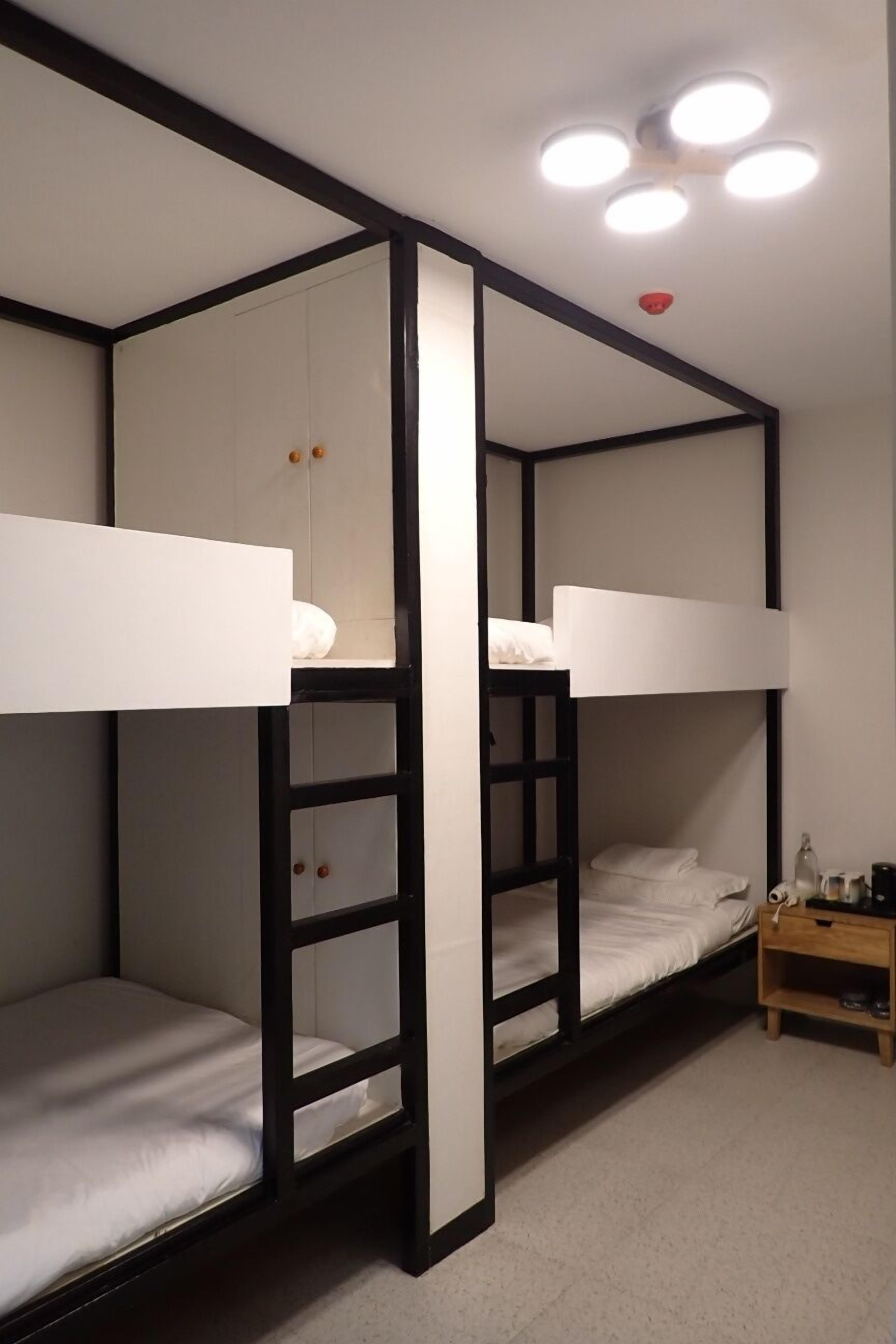 Ein Schlafzimmer mit Etagenbett, dessen Rahmen aus Holz ist, mit weißer Bettwäsche und einem kleinen Nachttisch mit Lampe.