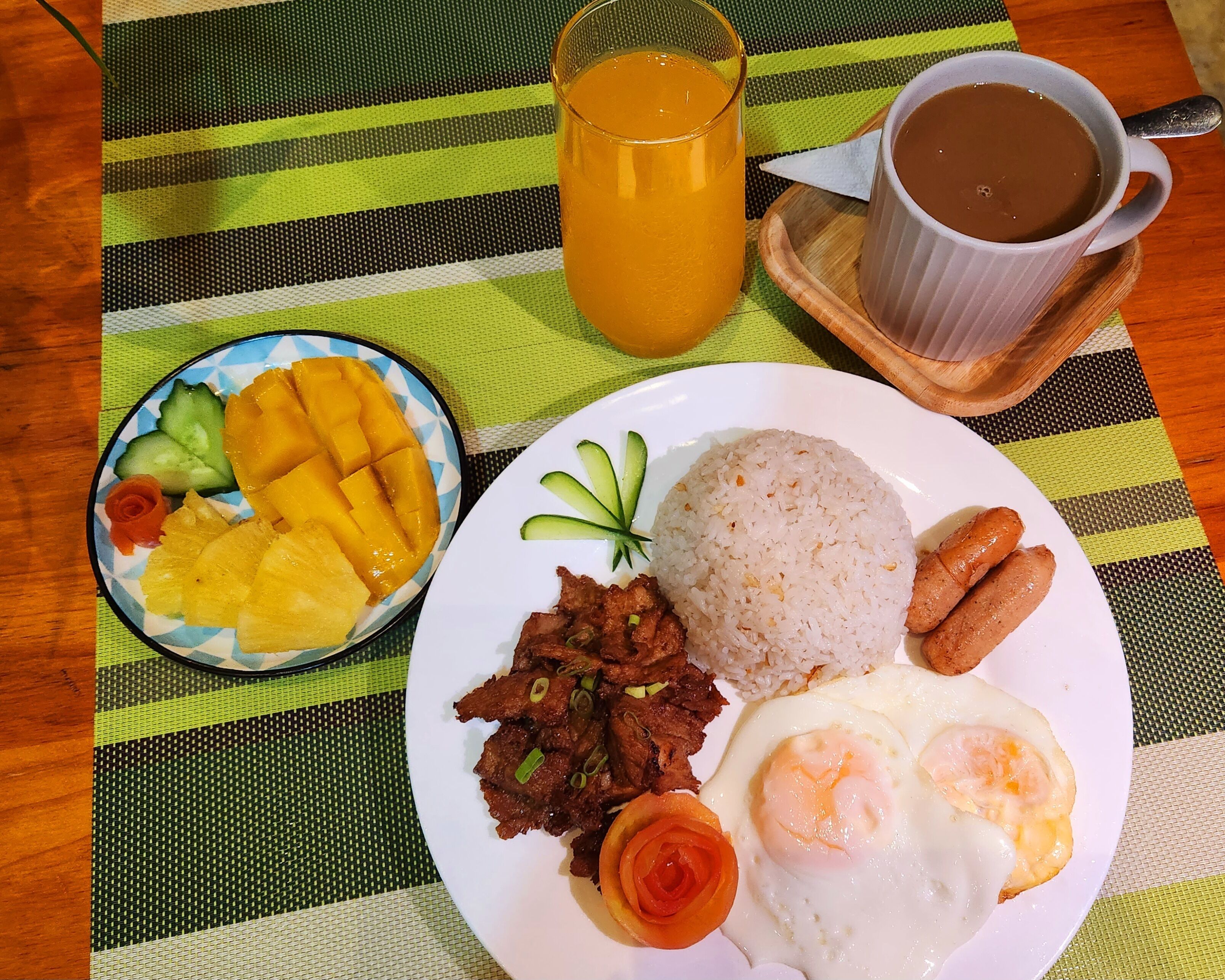 A plate with rice, eggs, meat, and vegetables, a glass of orange juice, and a cup of coffee on a striped tablecloth.