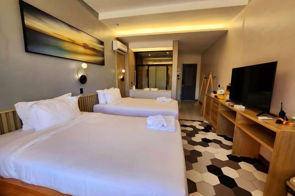 A hotel room with two beds, a TV, a desk, and a large painting on the wall.