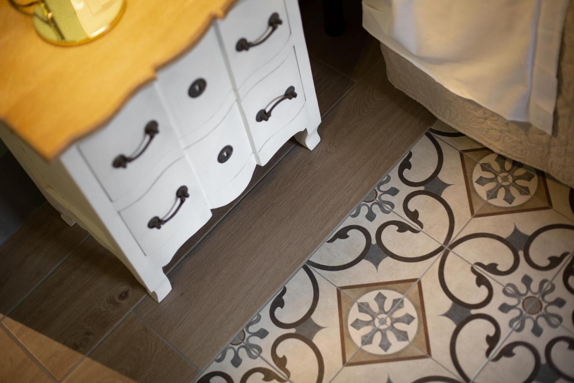A white dresser with multiple drawers and a wooden top, positioned next to a patterned floor.