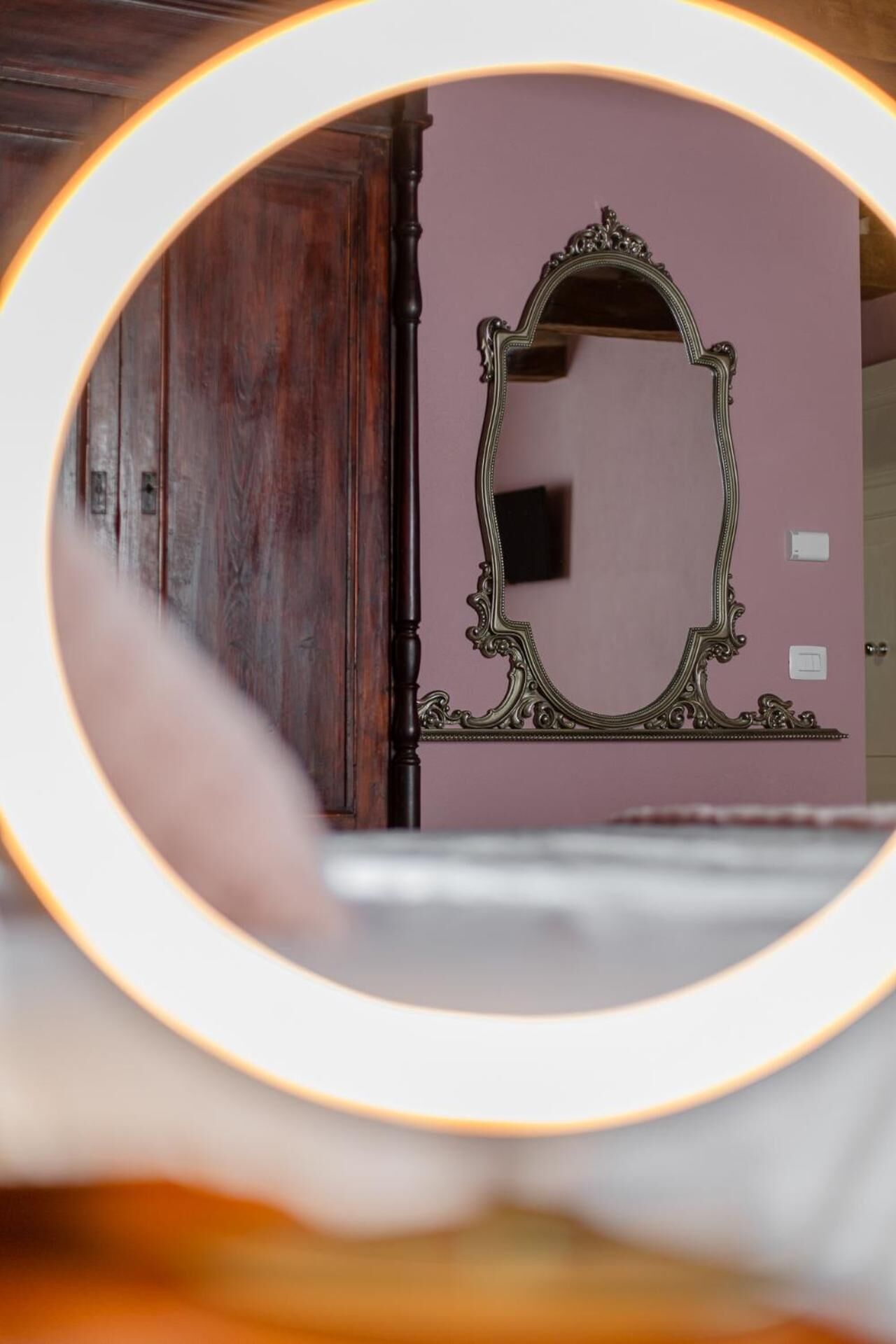 A mirror with an ornate frame, a wooden wardrobe, and a pink wall.