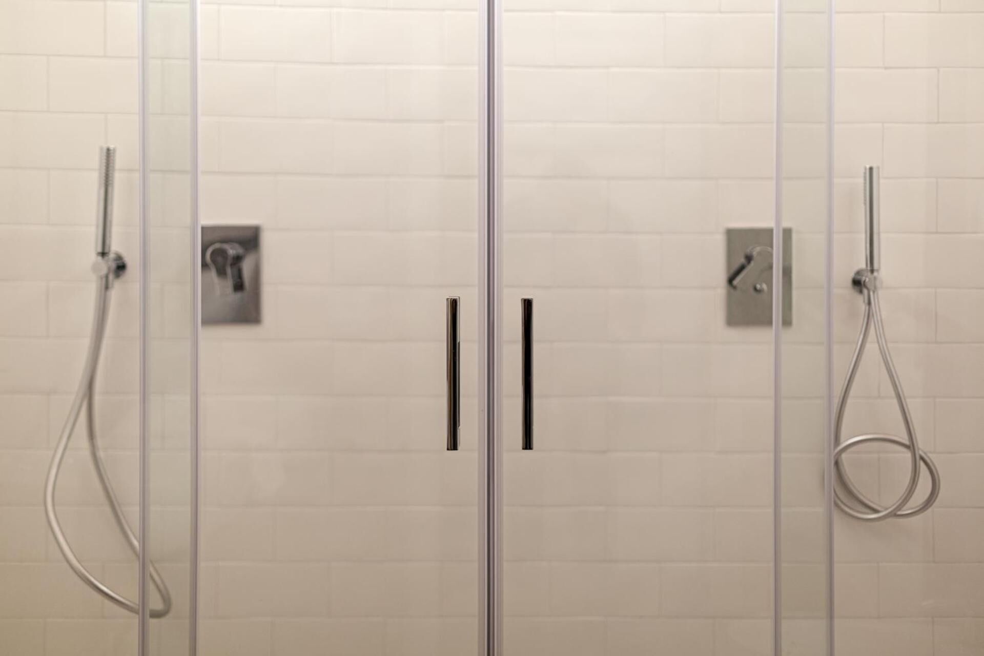 Baño con dos cabezales de ducha y una mampara de vidrio.