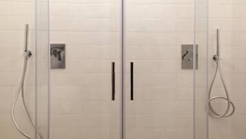 Baño con dos cabezales de ducha y una mampara de vidrio.