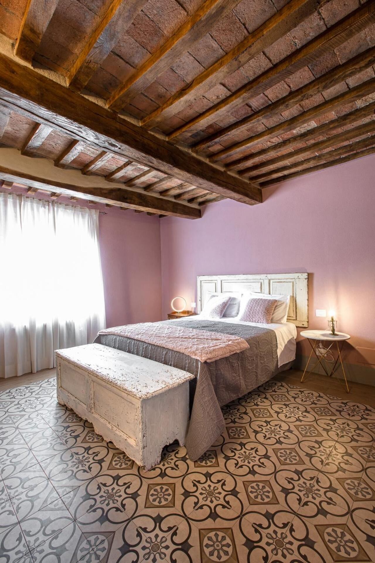 Un dormitorio con cama, mesitas de noche, un banco y suelo con baldosas estampadas.