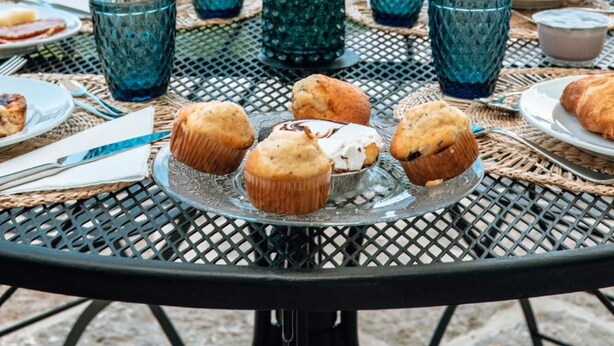 An outdoor dining table with blue glassware, a rose in a green vase, and muffins on a glass plate. - B&B Gli Archi (Abbadia San Salvatore)