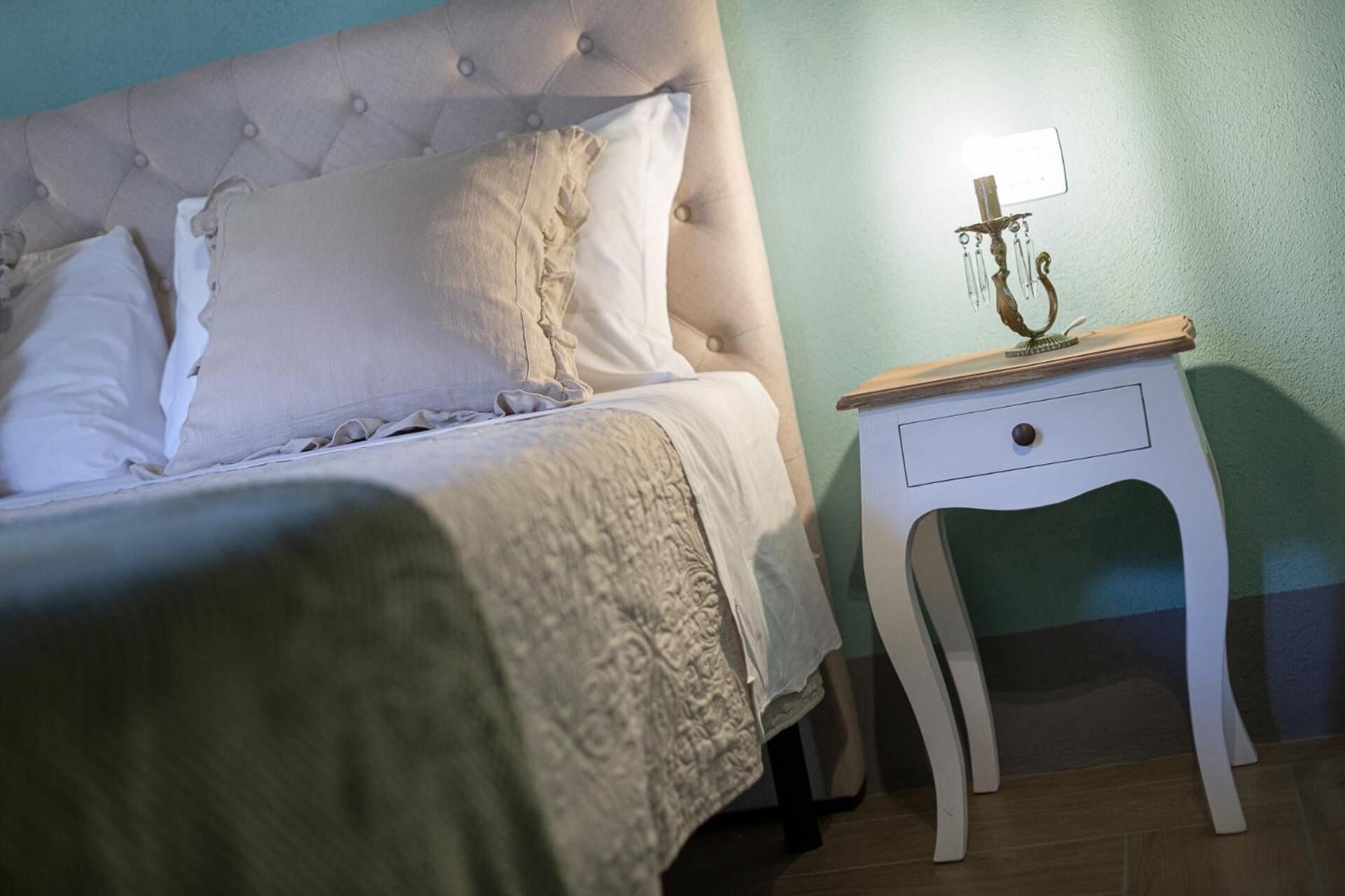 Un lit bien fait, avec une tête de lit capitonnée et une table de chevet sur laquelle se trouve une lampe.