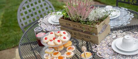 A round metal table with a floral centerpiece, a tray of pastries, and a honey jar.
