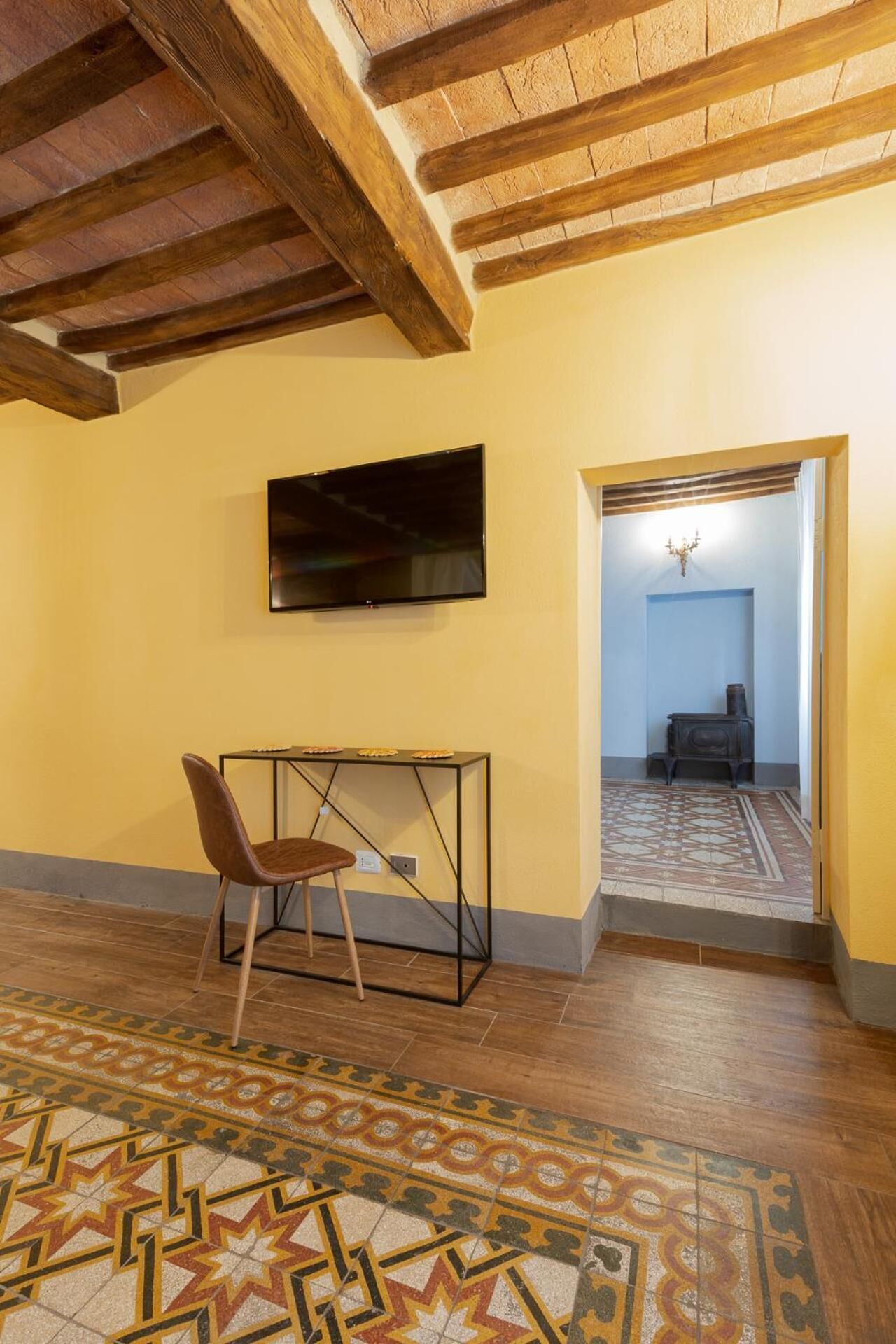 A room with a wooden ceiling, a television mounted on the wall, a patterned rug, and a chair.
