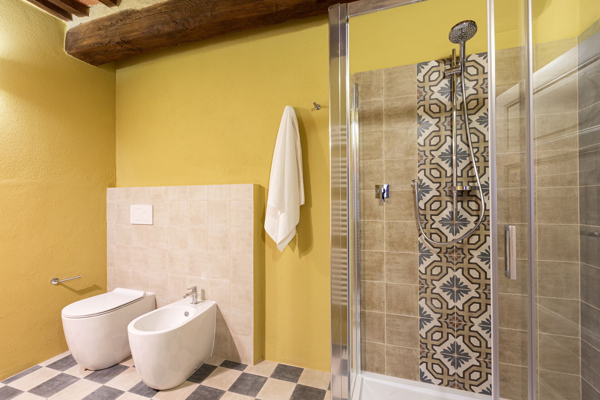 Casa de banho com sanita, bidé e chuveiro com azulejos estampados.