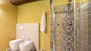 Casa de banho com sanita, bidé e chuveiro com azulejos estampados.