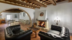 A rustic living room with exposed wooden beams, a fireplace, leather armchairs, and a dining area with a table and chairs. - B&B Gli Archi (Abbadia San Salvatore)
