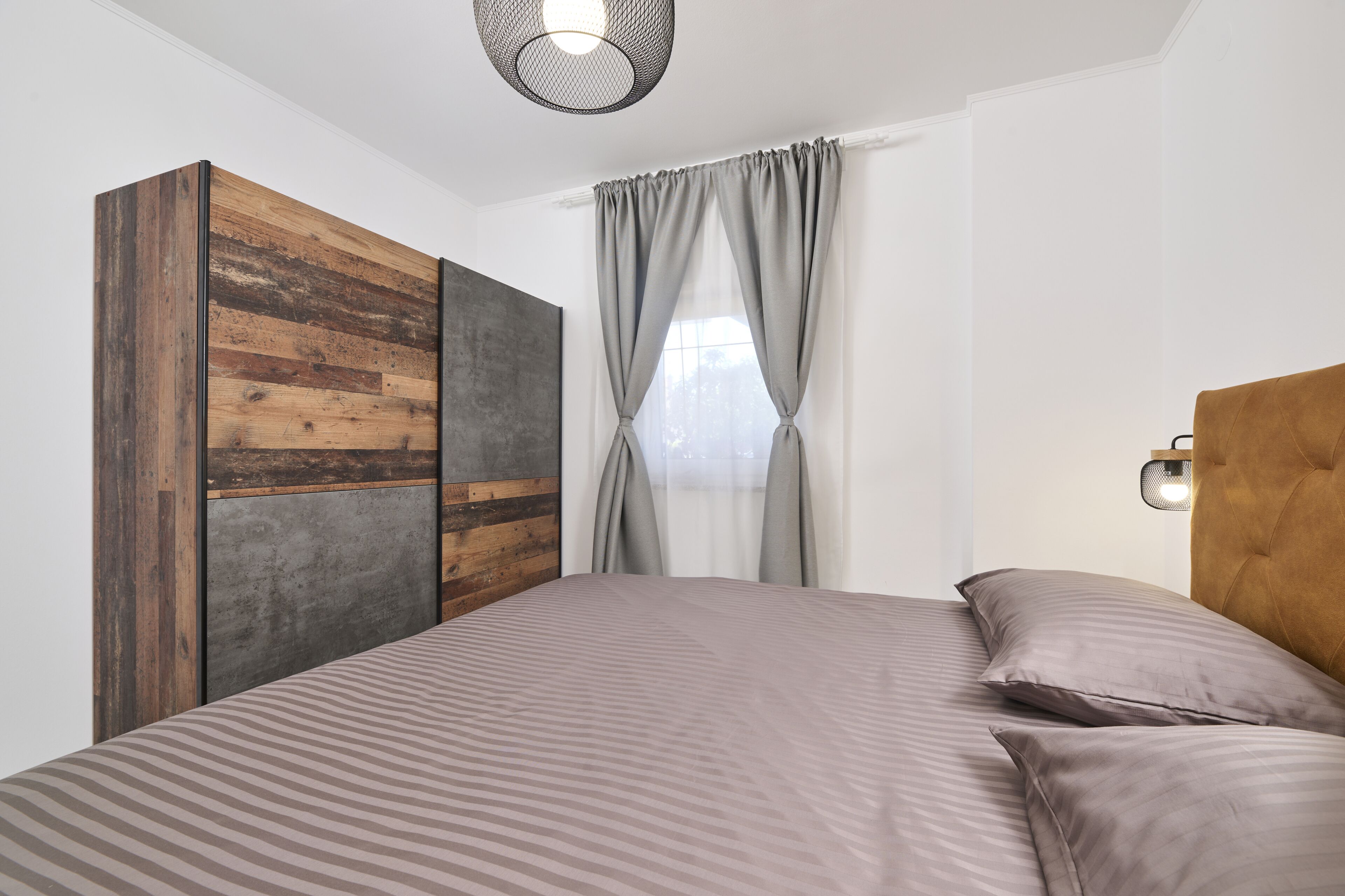 A bedroom with a bed, a wardrobe, and a window with curtains.