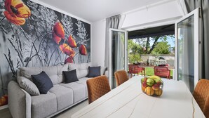 Uma sala de estar moderna com um sofá cinza, cadeiras laranja, uma mesa de jantar branca e uma fruteira.