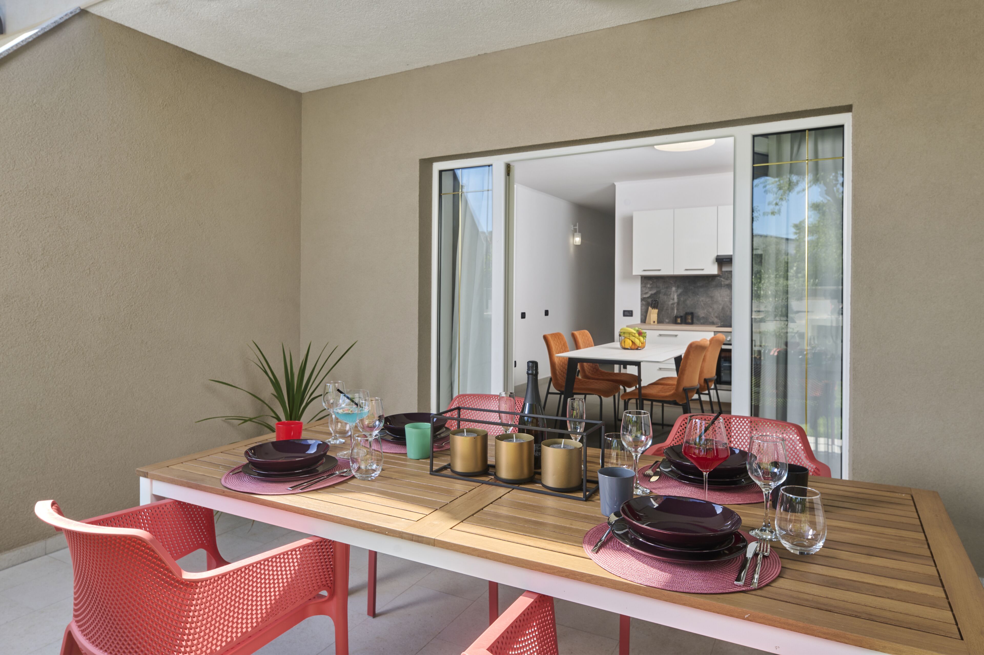 A dining area with a table set for four, including plates, cutlery, and glasses. There are chairs around the table, and a plant is visible on the table.