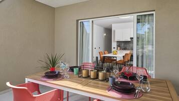 A dining area with a table set for four, including plates, cutlery, and glasses. There are chairs around the table, and a plant is visible on the table.