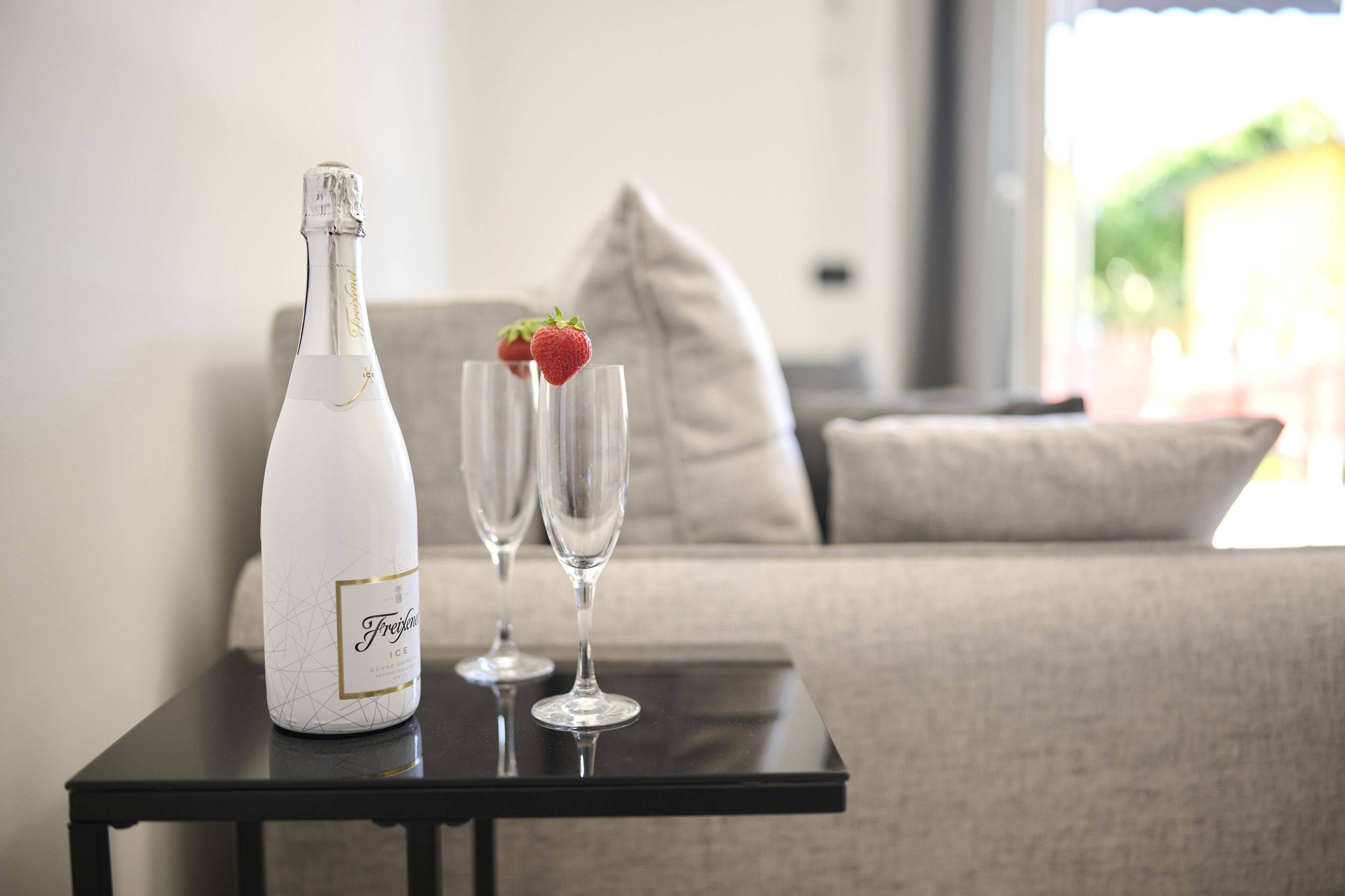 A bottle of Freixenet Ice on a table with two glasses, one with a strawberry.