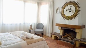 Una habitación de hotel con cama, una silla, chimenea y ventana con cortinas.