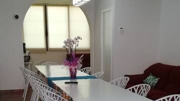 A dining area with a white table and chairs, a vase with flowers, and a red sofa.