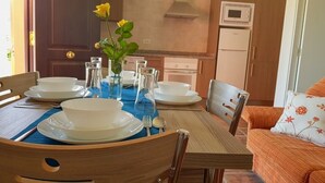 Una mesa de comedor dispuesta con platos y tazones blancos, un florero con flores amarillas y cristalería transparente.