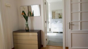 Un pasillo con un armario color beige, un jarrón con flores y un espejo en la pared.