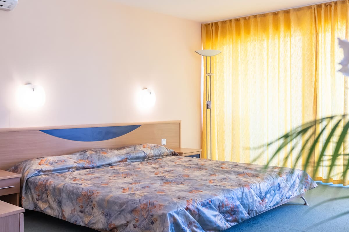 Habitación de hotel con cama, mesita de noche, lámpara y cortinas.