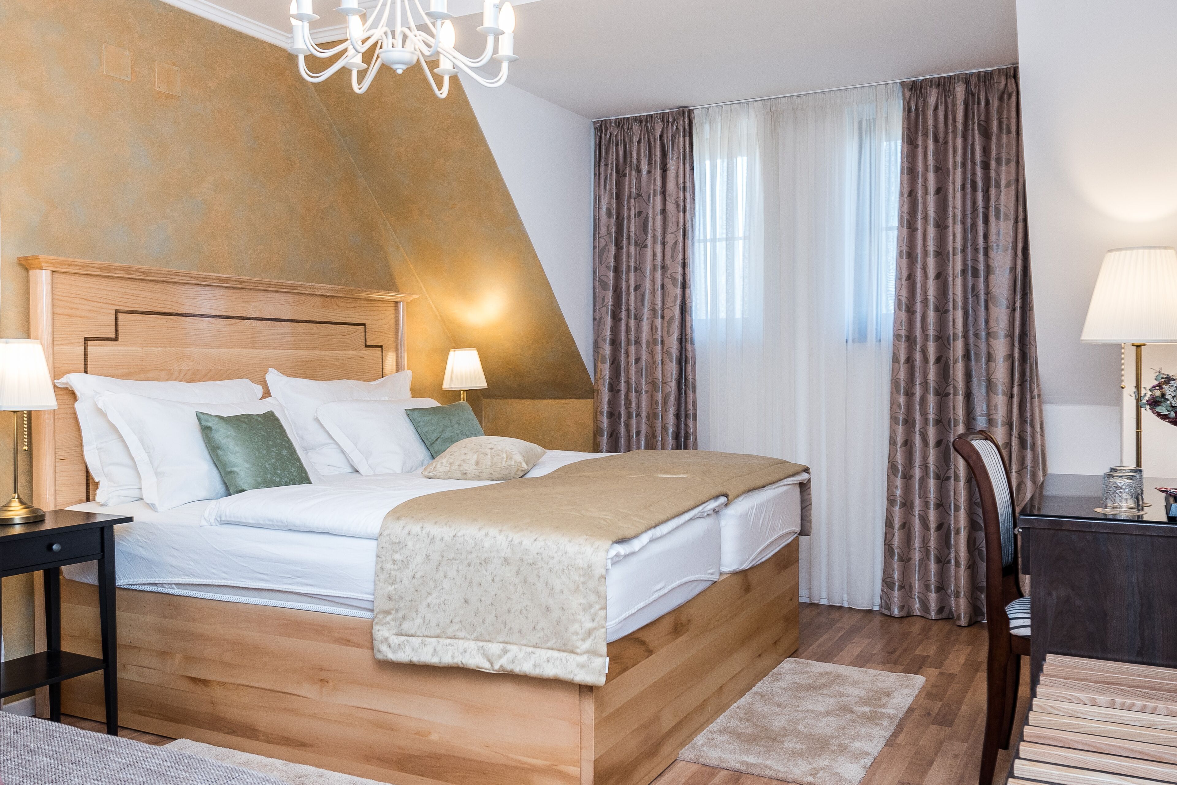 A bedroom with a wooden bed, two bedside tables, a chandelier, and a view of the outdoors through curtains.