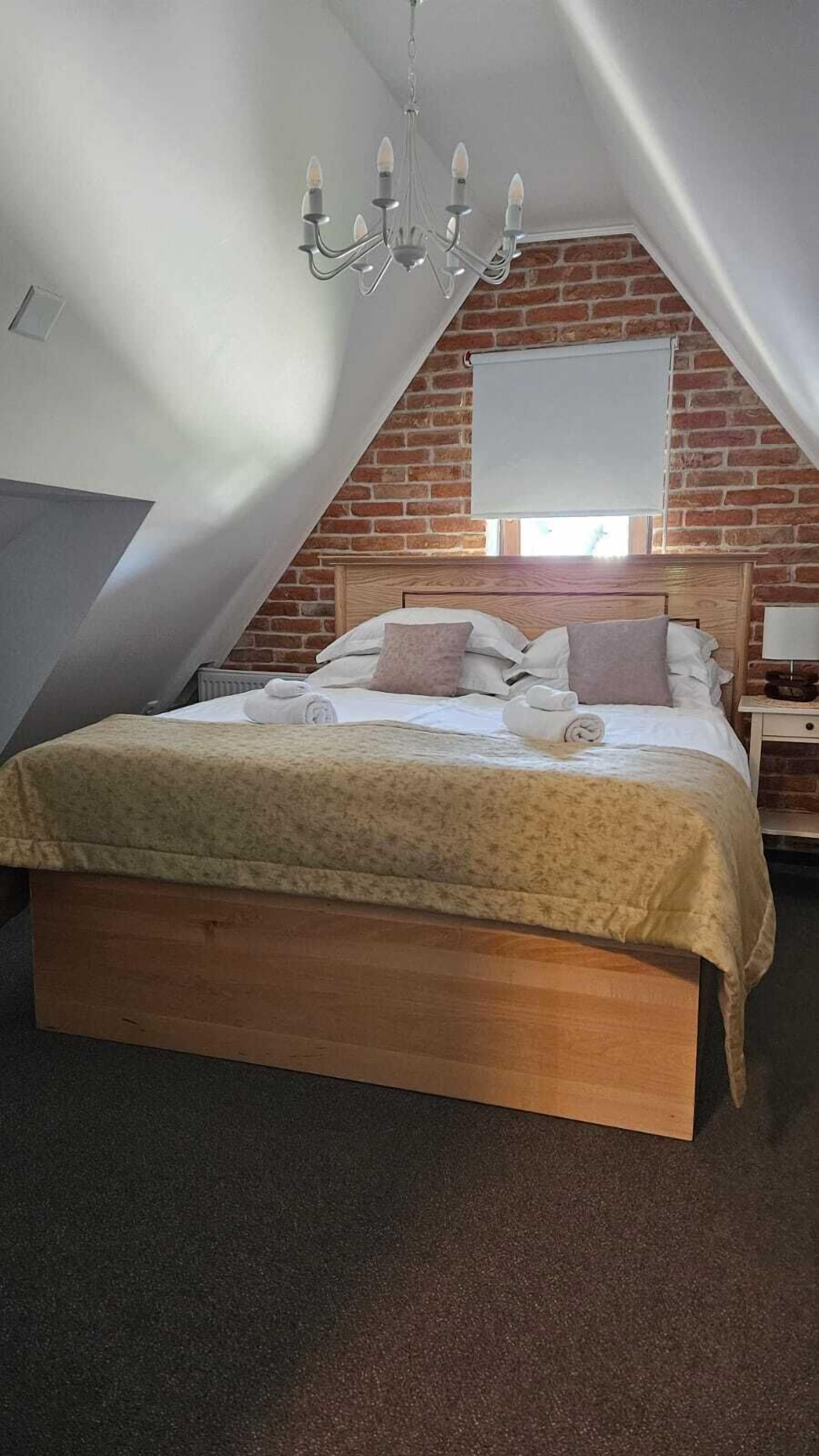 A bedroom with a wooden bed, a chandelier, a brick wall, and a window with a blind.