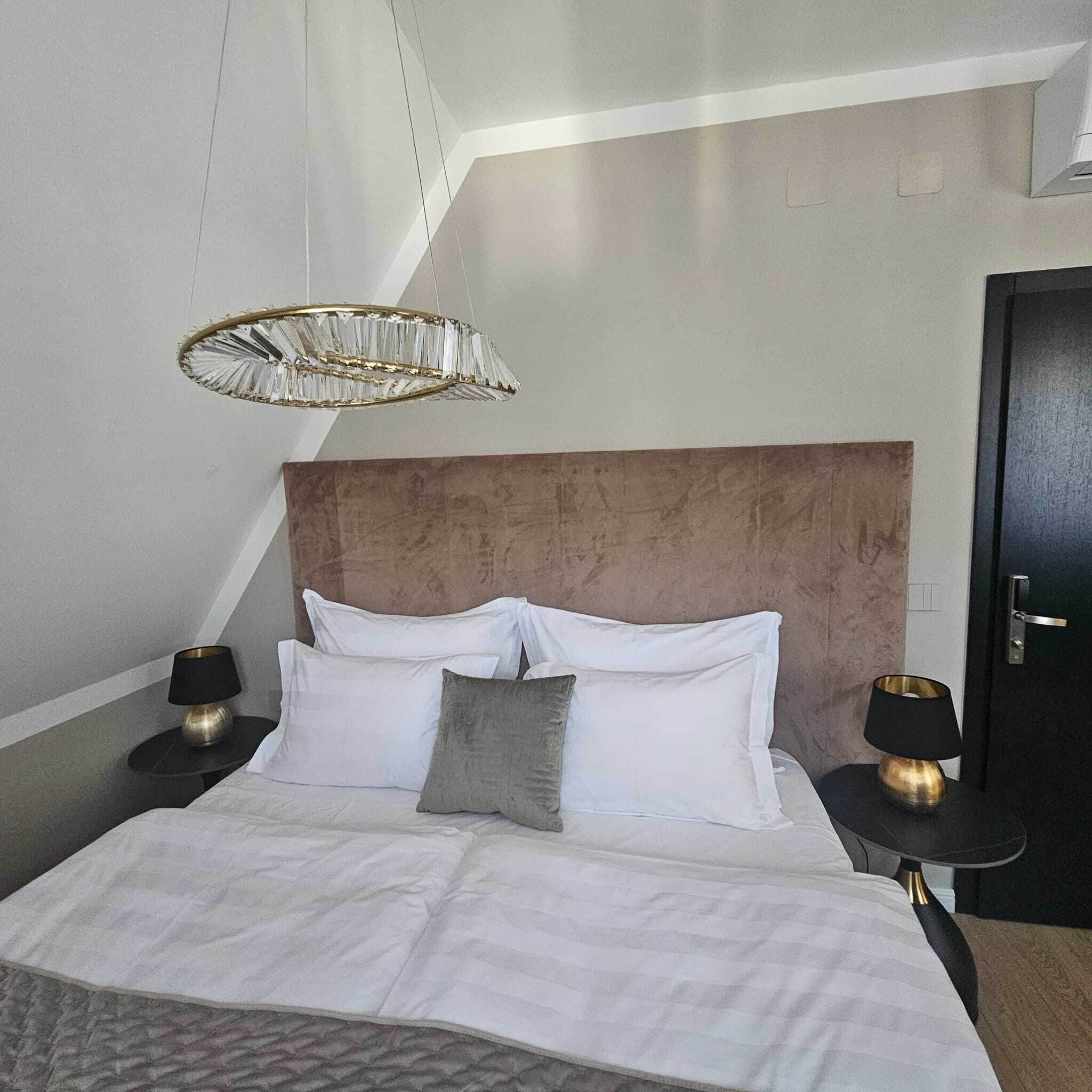 A modern bedroom with a large bed, two bedside tables, a unique geometric ceiling light, and a dark door.