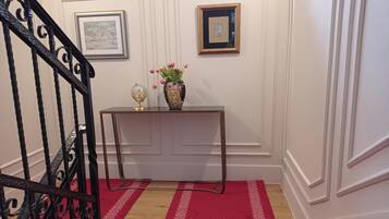 A staircase with a red carpet, a console table with a vase of flowers, and framed pictures on the wall.