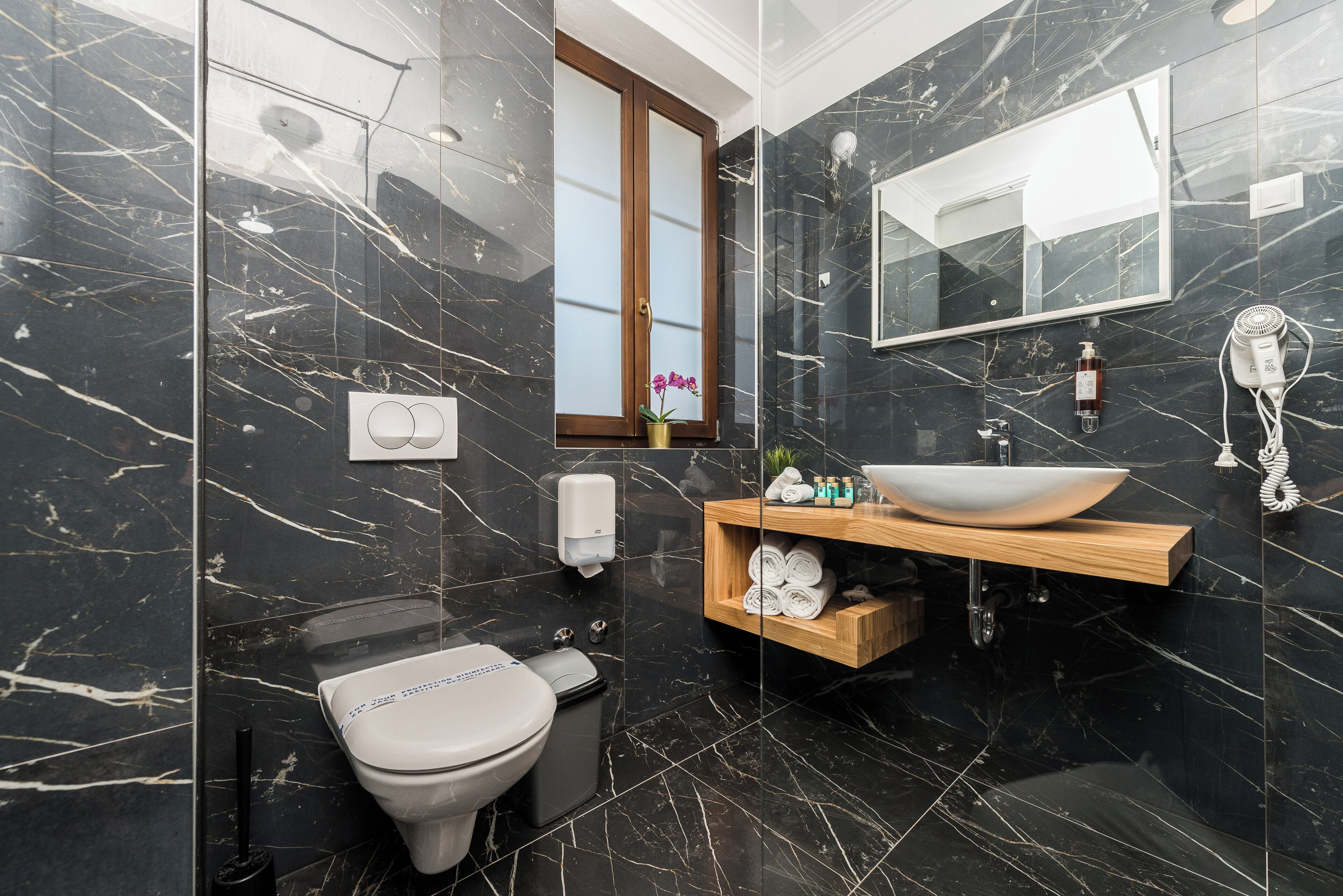 Een moderne badkamer met een marmeren vloer, een houten wastafelmeubel, een witte wastafel en een toilet.