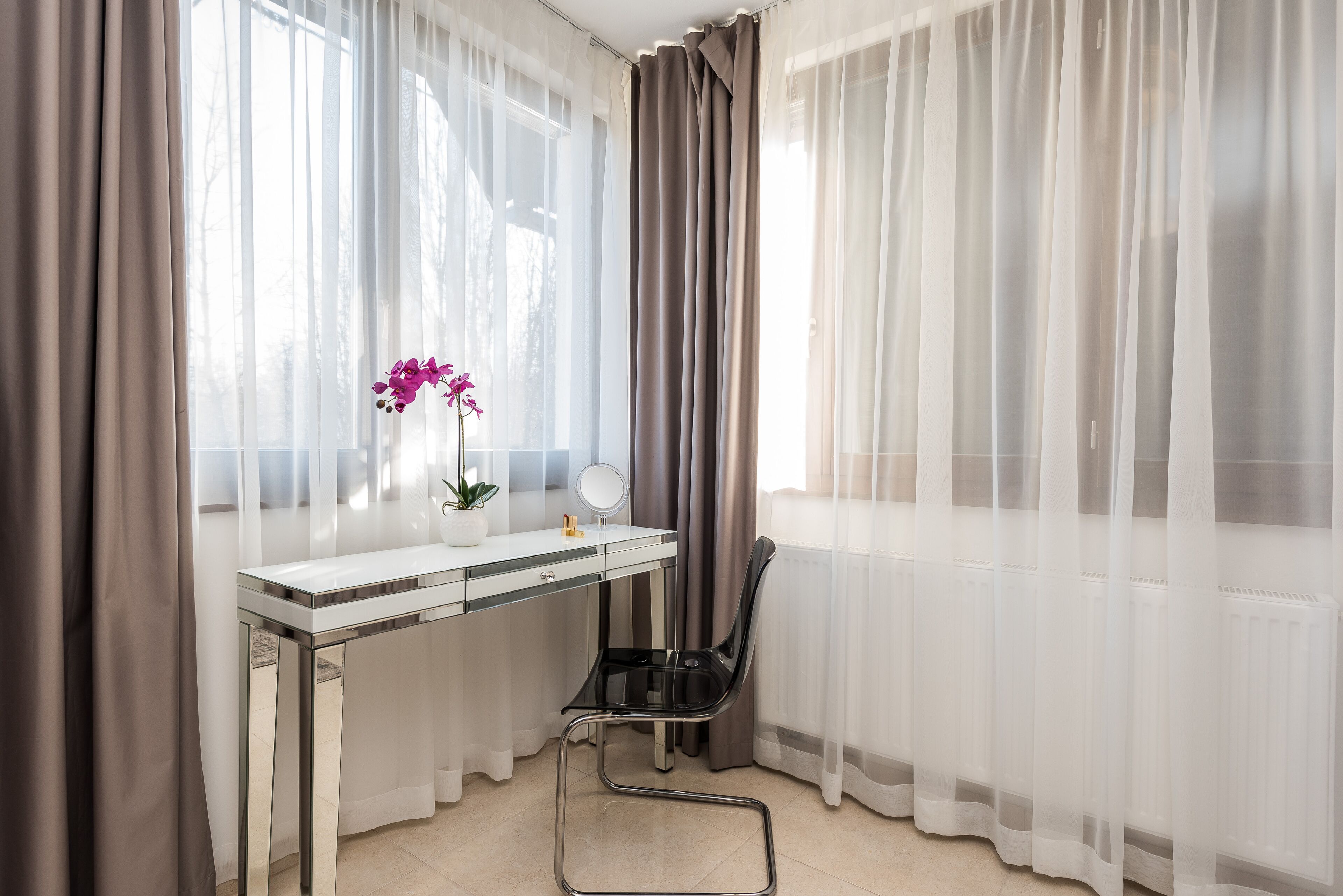 Una habitación con un escritorio blanco, una silla, una planta en maceta y cortinas de gasa.