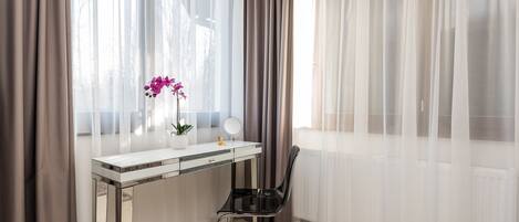 Una habitación con un escritorio blanco, una silla, una planta en maceta y cortinas de gasa.
