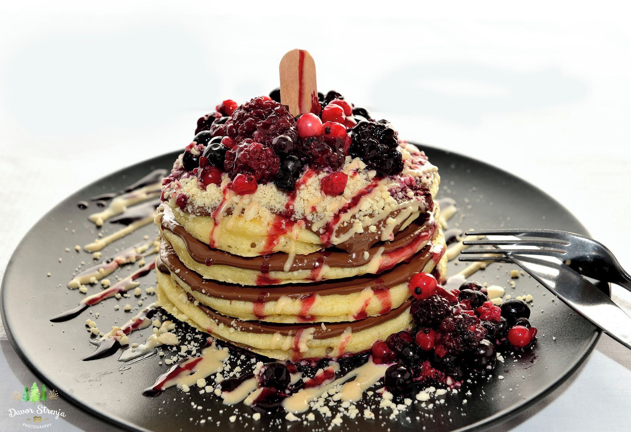 A stack of pancakes with berries and chocolate on a plate.