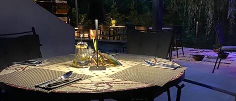 An outdoor patio with a round table set for dining, surrounded by chairs, and an umbrella providing shade.