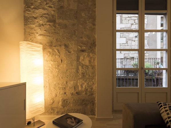 Une pièce avec un mur en pierre, une fenêtre donnant sur l’extérieur et une lampe sur une table.