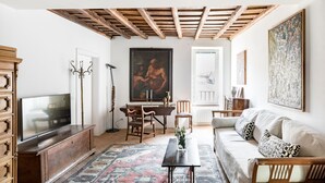 Una sala de estar con televisor, muebles de madera, alfombra estampada y obras de arte en las paredes.