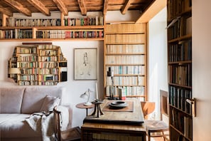 A cozy reading nook with a wooden bookshelf, a framed artwork, a comfortable sofa, and a small table with a lamp.