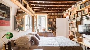 Una habitación acogedora con una cama, estanterías, un televisor y un escritorio con una lámpara.