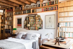 A cozy bedroom with a large bed, a wooden ceiling, and bookshelves filled with books.