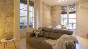 Ein modernes Wohnzimmer mit einem beigen Sofa, einem kleinen runden Tisch und einer Wand mit Steinoptik.