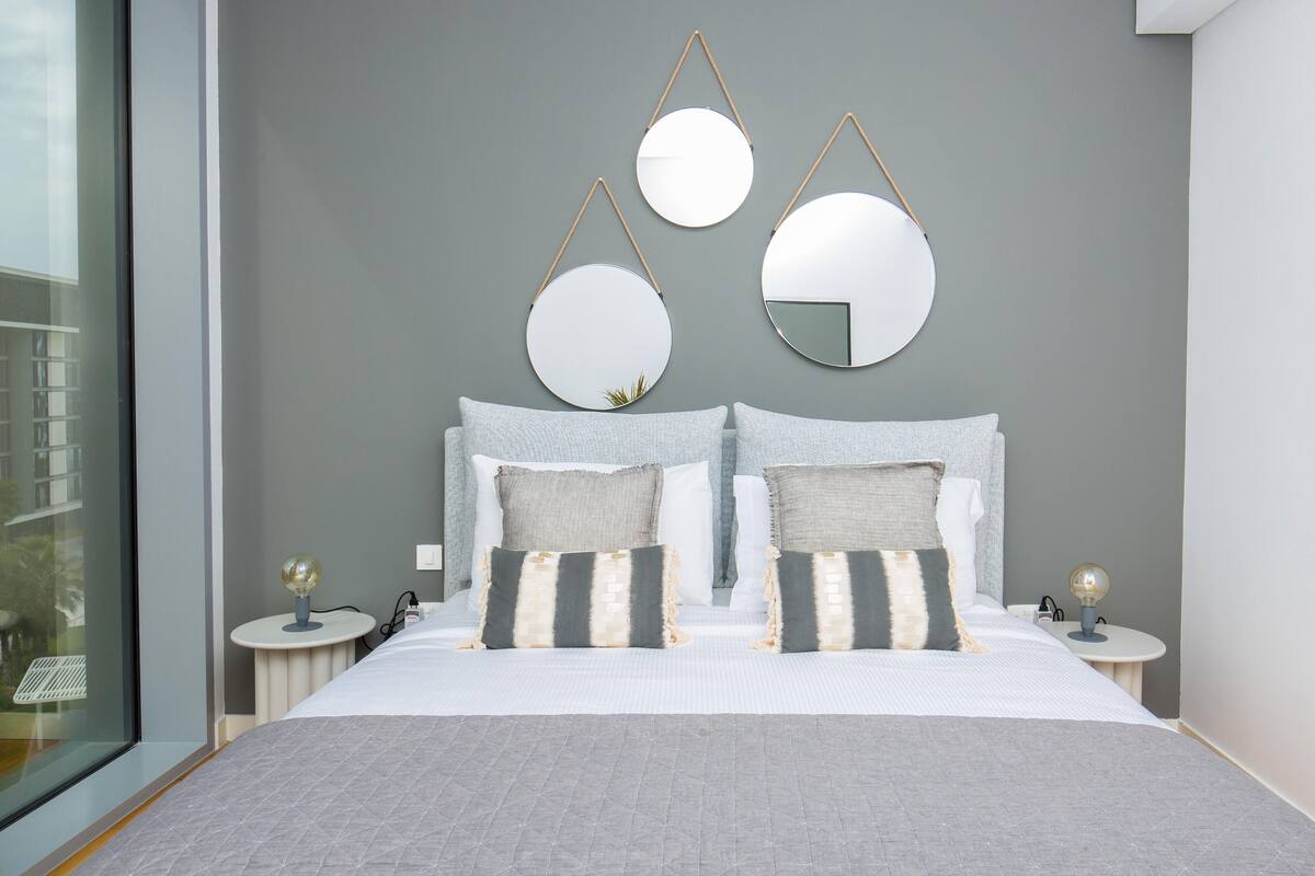 A modern bedroom with a large bed, grey walls, and three round mirrors on the headboard.