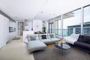 A modern living room with a sectional sofa, a coffee table, and a view of the city through large windows.