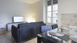Ein modernes Wohnzimmer mit einer Couch, einem Fernseher, einem Esstisch mit Stühlen und einer Steinwand.