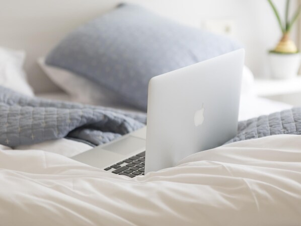 A laptop on a bed with a white and blue blanket.