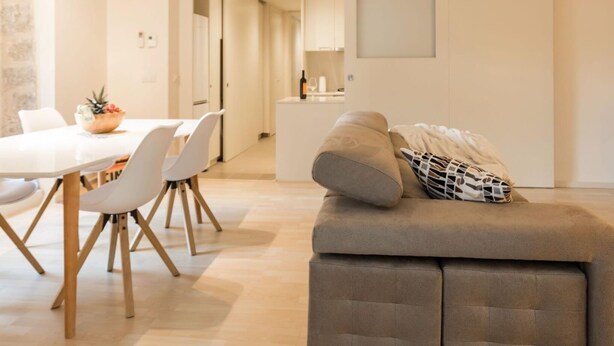 A modern living room with a sofa, dining table, and chairs. There is a kitchen area in the background. - Bravissimo Cort Reial 3B, fantastic apartment (Girona)