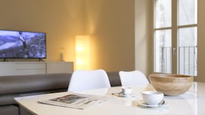 A modern living room with a white sofa, a dining table with a bowl and cups, a television, and a window with a view. - Bravissimo Cort Reial 3B, fantastic apartment (Girona)