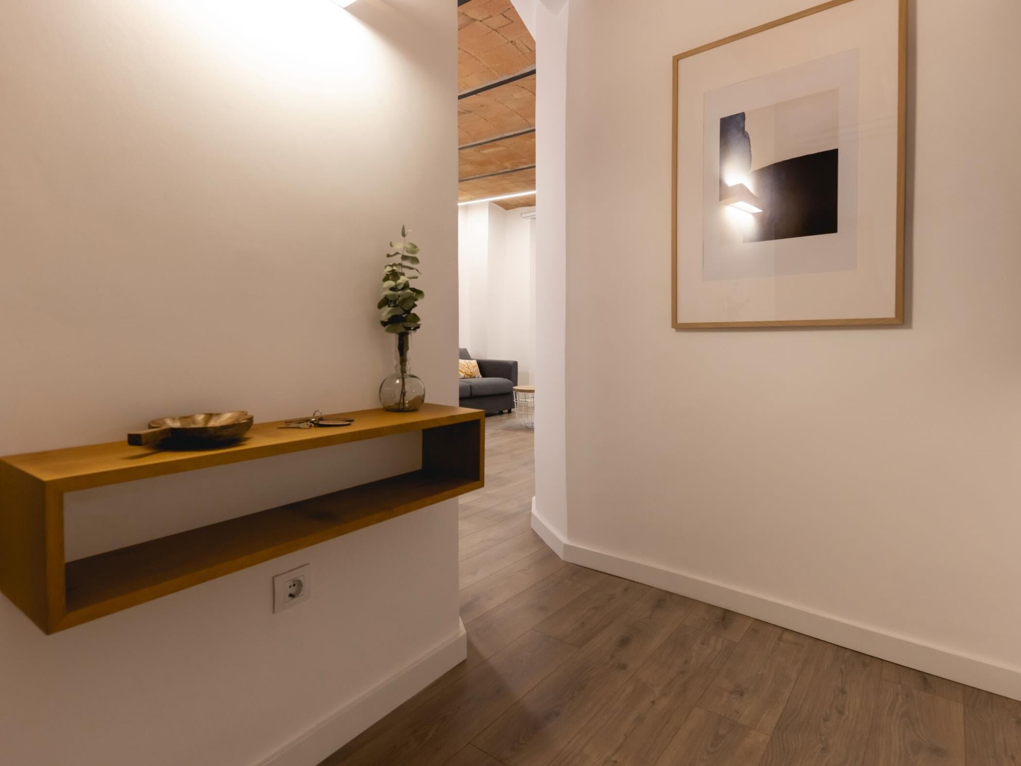 A hallway with a wooden console table, a vase with a plant, and a framed artwork on the wall.